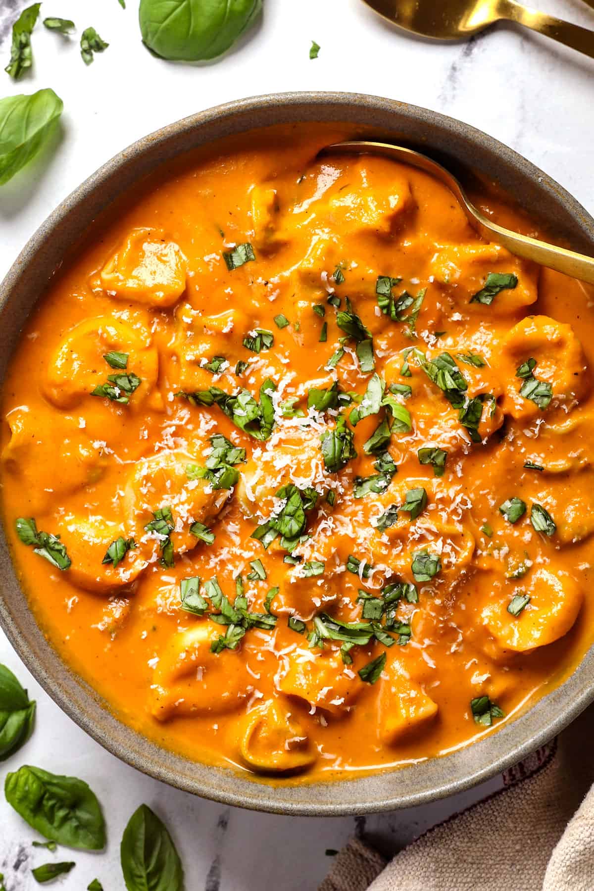 A bowl of creamy tomato tortellini soup topped with fresh basil and grated parmesan